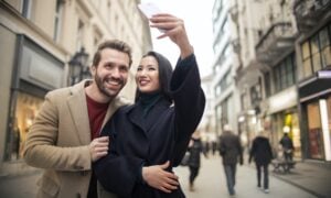 A man and woman take a selfie on a city street.