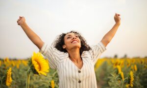 A happy woman with outstretched arms in a field of sunflowers.