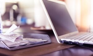 An open laptop on a table beside a pile of receipts.