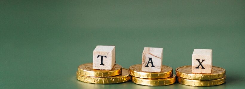 Three wood blocks spelling TAX sit on piles of gold coins