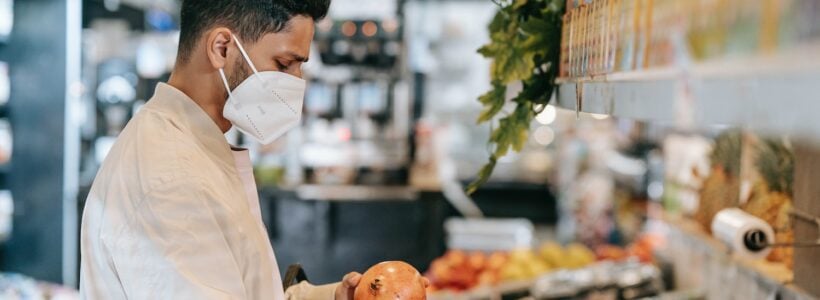 A man picks up an onion while shopping for groceries.