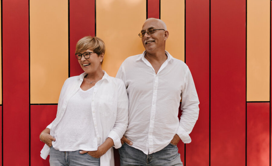 A older couple is seen happily posing in front of a wall.