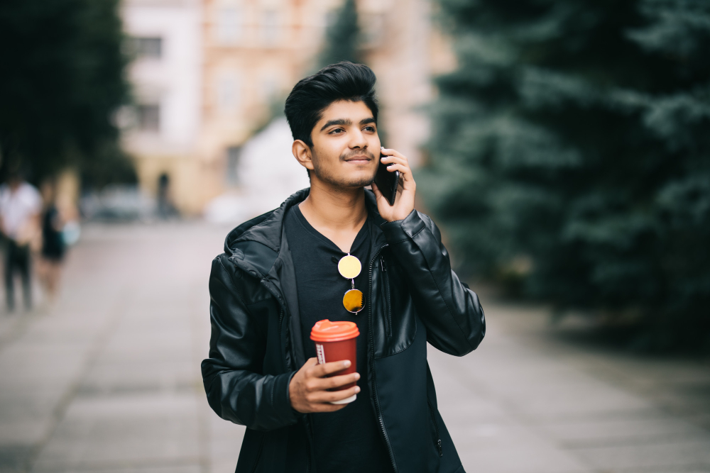 A young Indian man talks on his phone and holds a coffee cup