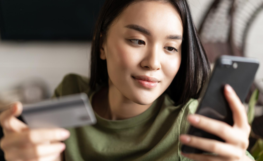 A young woman looks at her phone and holds a credit card