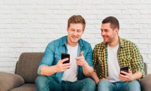 Two smiling young men check their accounts on their phones