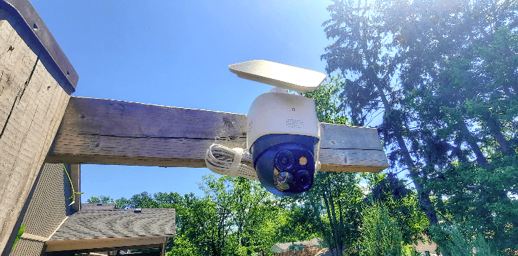 A security camera with a solar panel, mounted on a backyard deck