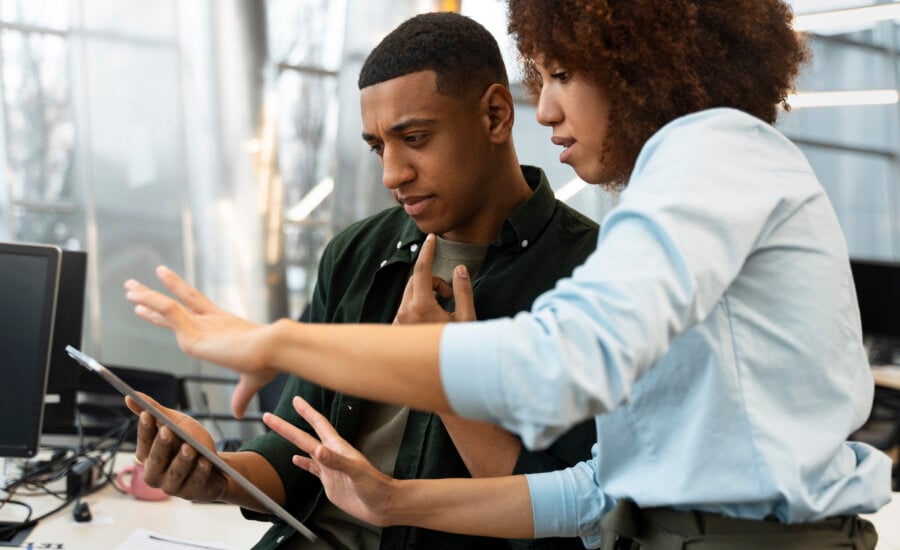 An image of two people looking into an ipad while in an office setting.