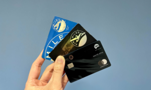 A hand holds up 2 Air Miles cards and a BMO Air Miles Mastercard