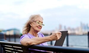 A senior-age woman looks at her tablet on a park bench.