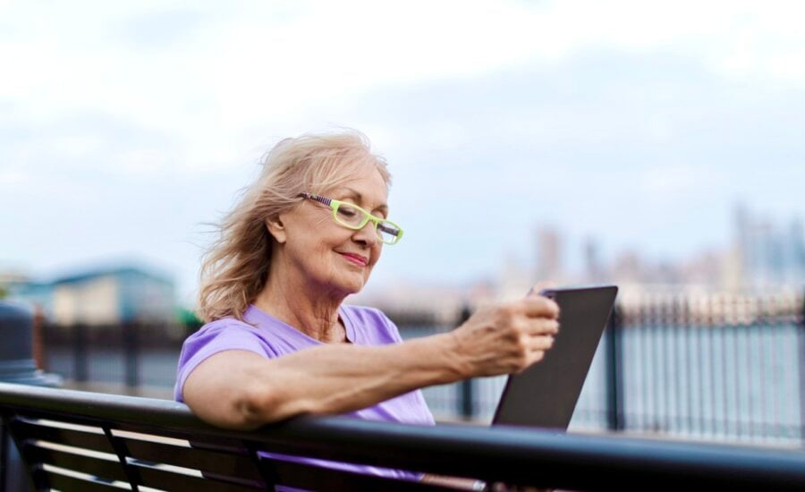 A senior-age woman looks at her tablet on a park bench.