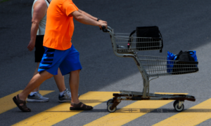 Two men push a shopping cart across a parking lot