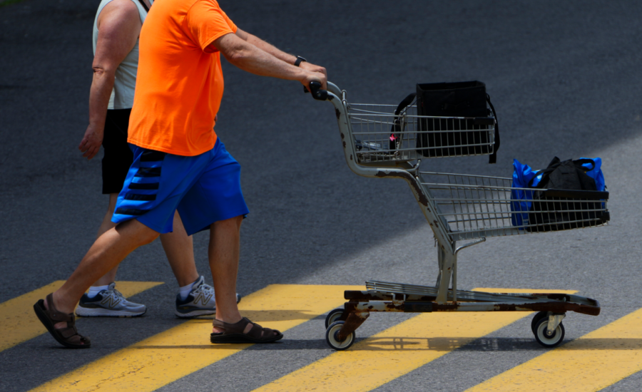 Two men push a shopping cart across a parking lot