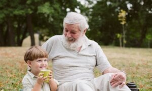 A man sits in the grass with this grandson, who is drinking from a cup