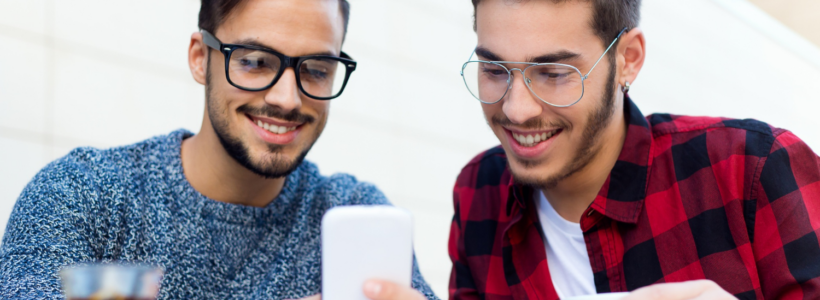 Two young people at a cafe smile at a smartphone.