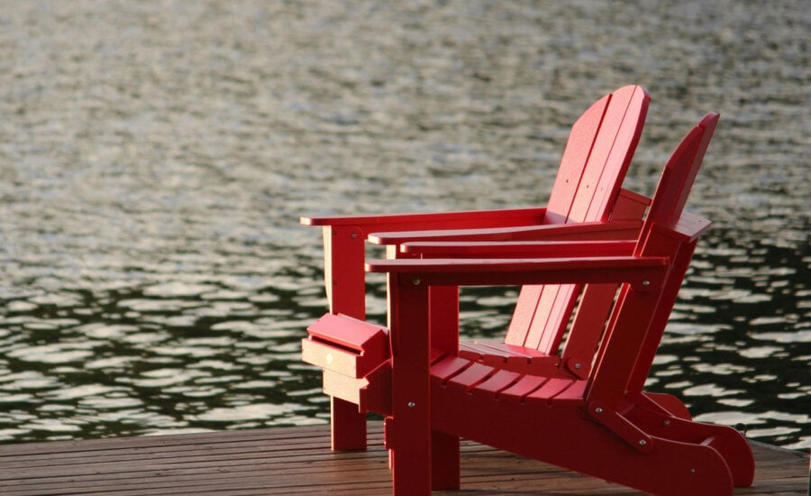 Two empty Muskoka chairs on a deck, to inspire the contrast of the perks of a cottage in Canada and the financial implications.