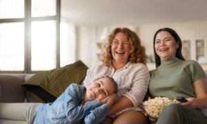 Two women and a young girl laying cross them laugh while watching TV