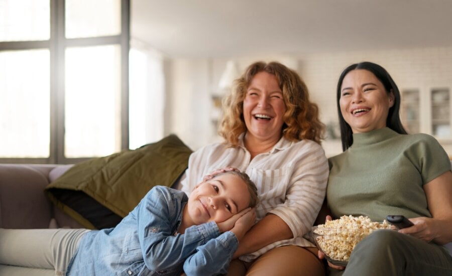 Two women and a young girl laying cross them laugh while watching TV