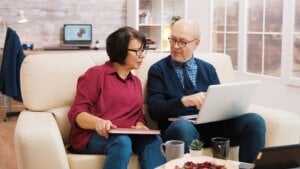 Elderly age couple using laptop while sitting on sofa in living room