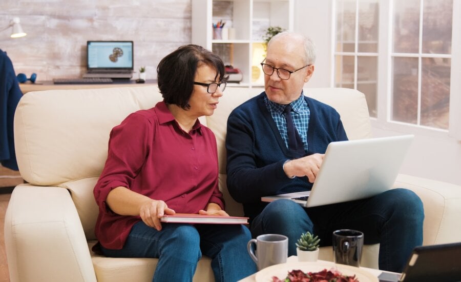 Elderly age couple using laptop while sitting on sofa in living room