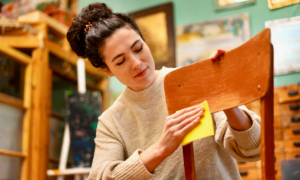 A woman refinishes a wooden chair