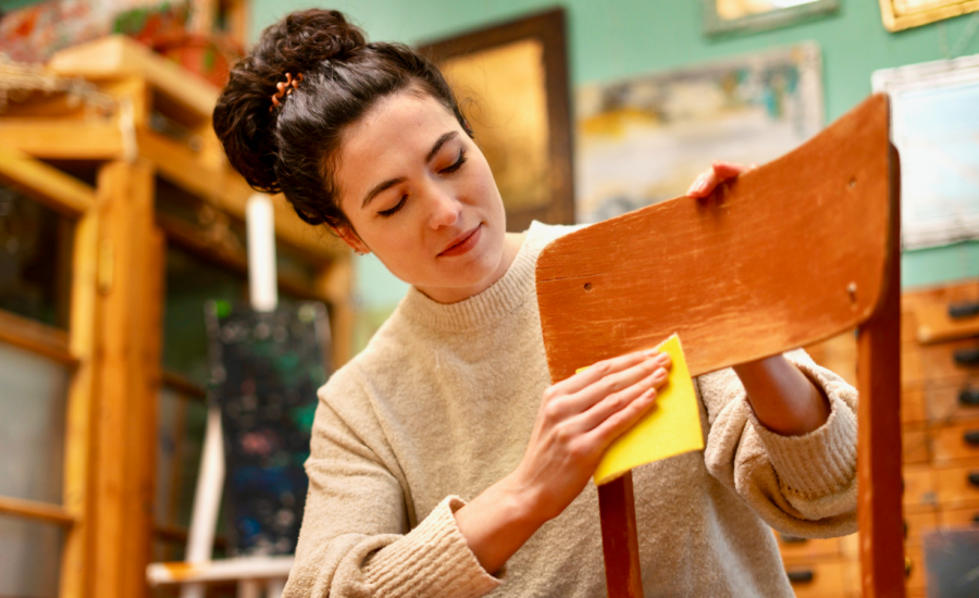 A woman refinishes a wooden chair