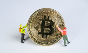 2 figurines of miners hold a golden Bitcoin coin