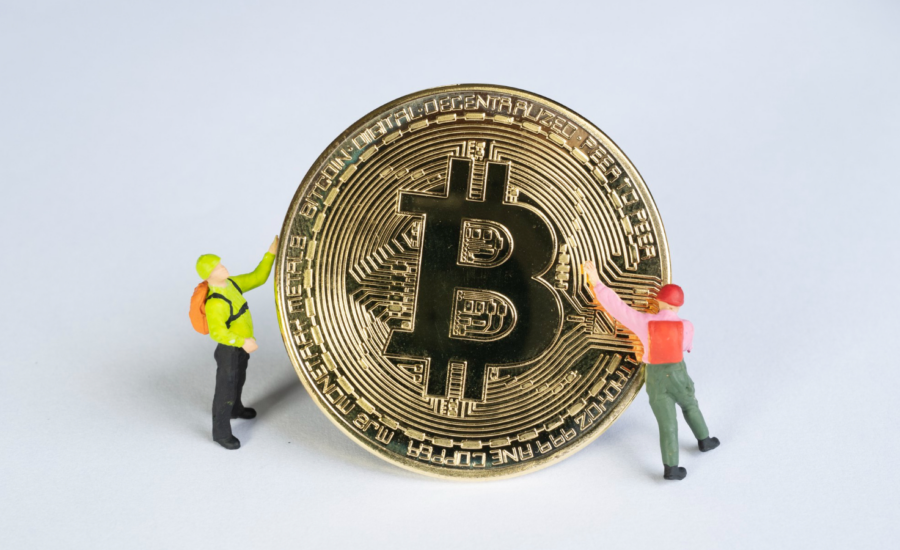 2 figurines of miners hold a golden Bitcoin coin