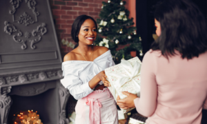 A woman gives another woman a wrapped holiday gift