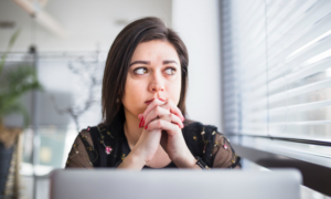 A woman looks worried as she sits in front of her laptop.