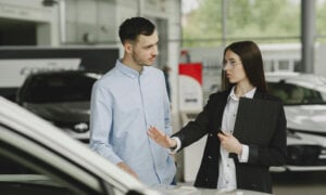 Newcomer to Canada buying their first car at the dealership asking questions of the sales person about getting a car loan.