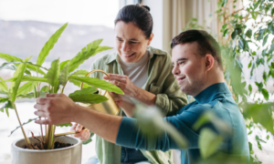 A young man with Down syndrome helps a woman water a house plant