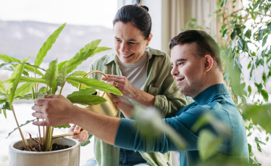 A young man with Down syndrome helps a woman water a house plant