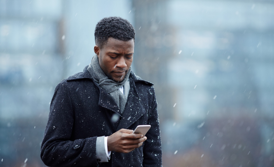 A young man checks his phone while walking in the snow