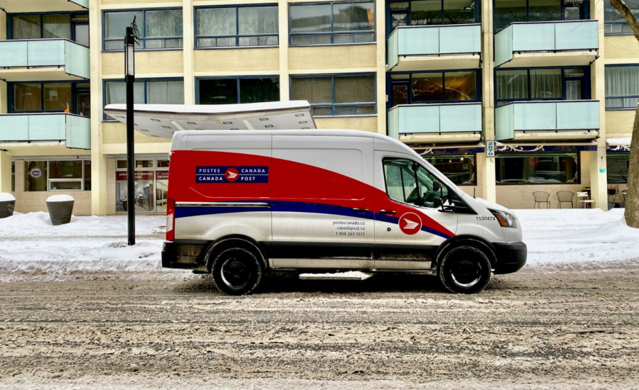 A Canada Post truck on a snowy street in front of an apartment building