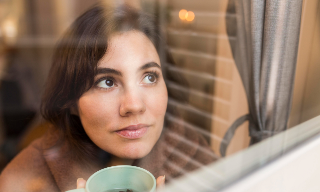 A woman looks hopefully out the window while drinking tea