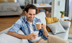 Smiling man on a sofa holding a phone and a coffee mug