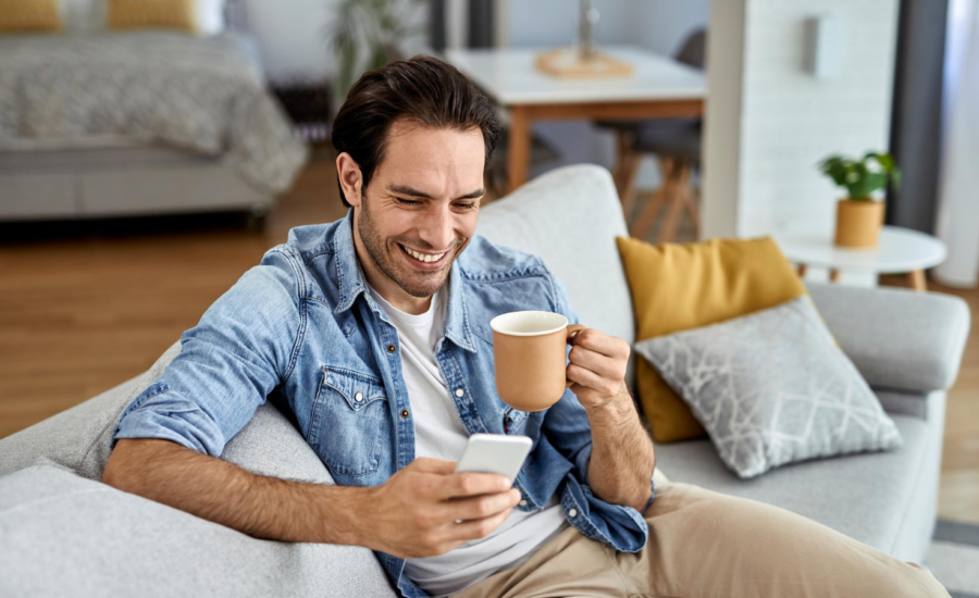 Smiling man on a sofa holding a phone and a coffee mug