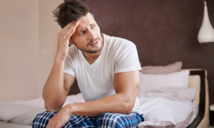 A worried young man in pajamas sits on his bed