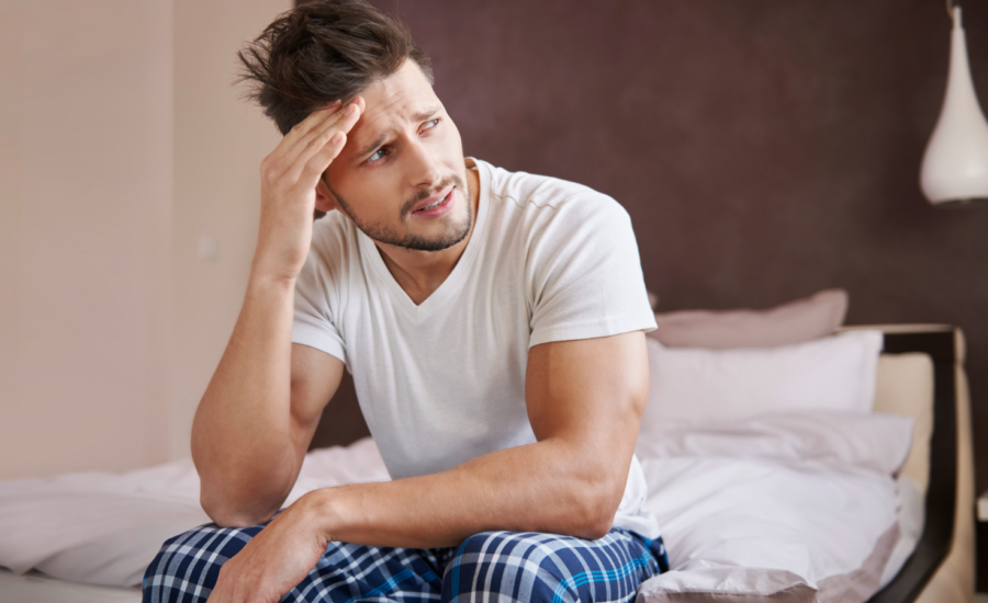 A worried young man in pajamas sits on his bed