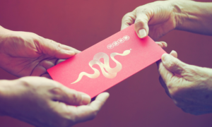 Close-up of hands giving a lucky money envelope with a gold snake design