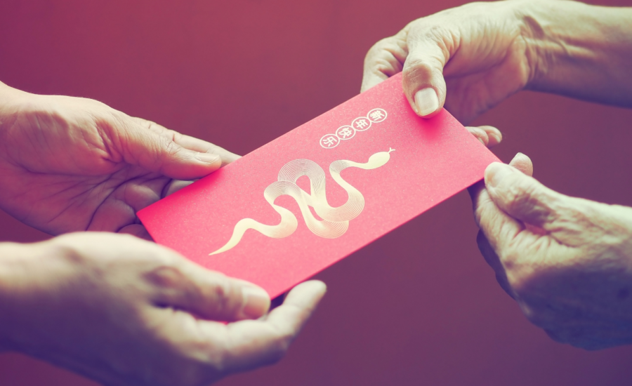 Close-up of hands giving a lucky money envelope with a gold snake design