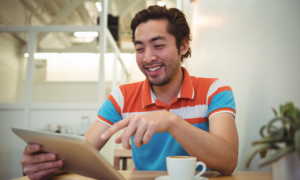 A smiling man uses his tablet in a cafe