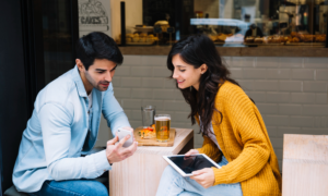 A man and woman look at a phone in a cafe