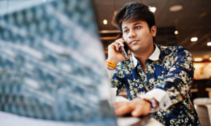 A young man uses his phone and laptop in a cafe