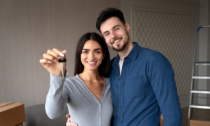 A smiling young couple hold a key in their new home